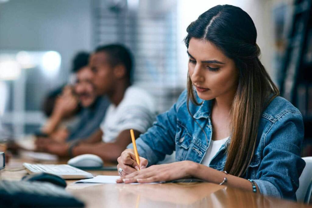 a medical student sits at a desk and writes on paper with a pencil