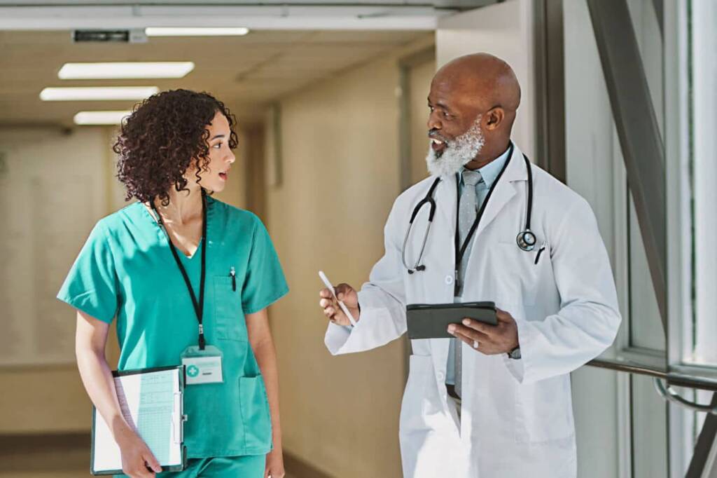 medical student in green scrubs walks down a hall and talks with a doctor in a white coat