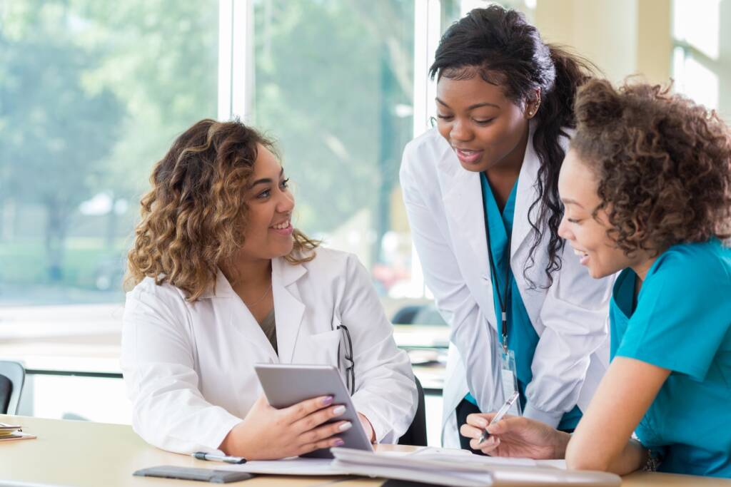 Three female medical students collaborate at a table, discussing notes and sharing ideas in a study session.