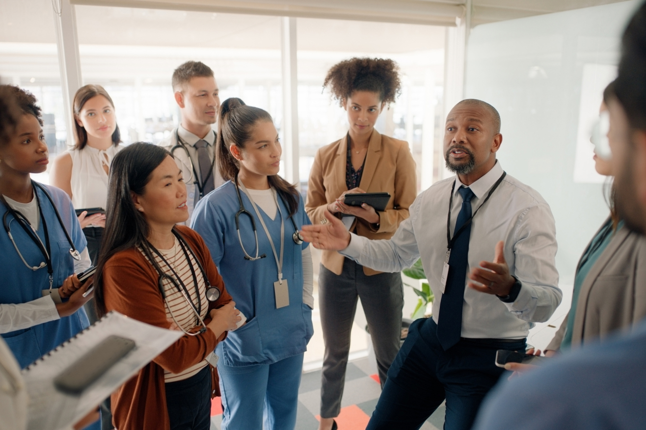 A group of healthcare professionals in scrubs engaged in conversation in a clinical setting.