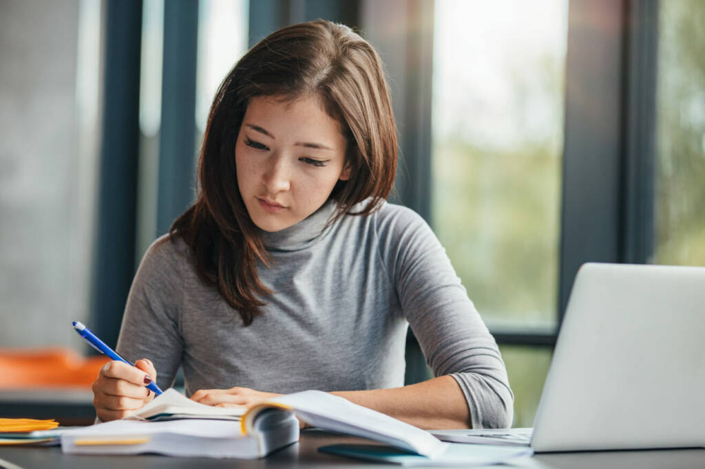 2. A woman is seated at a table, using a pen to write notes in her notebook.