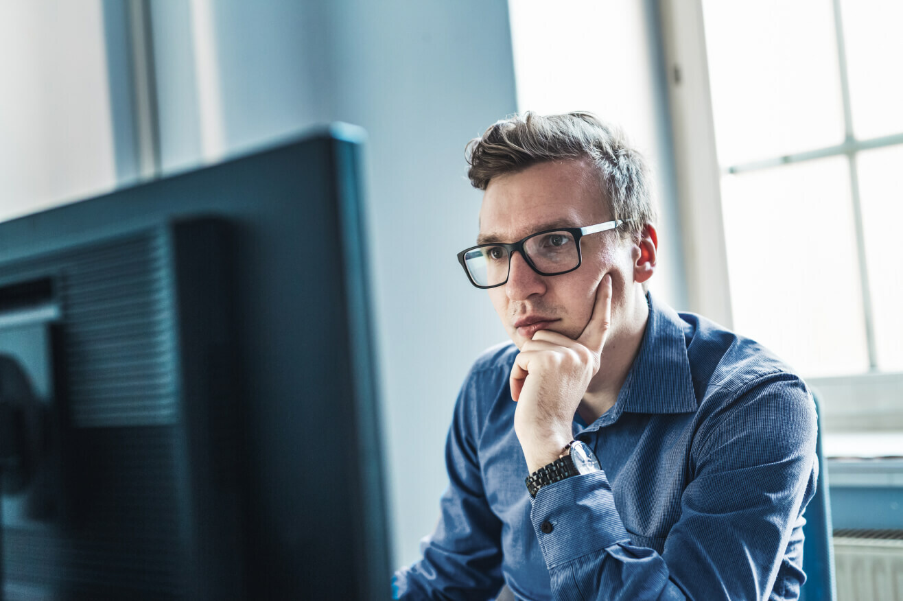 A man wearing glasses is intently focused on a computer screen.