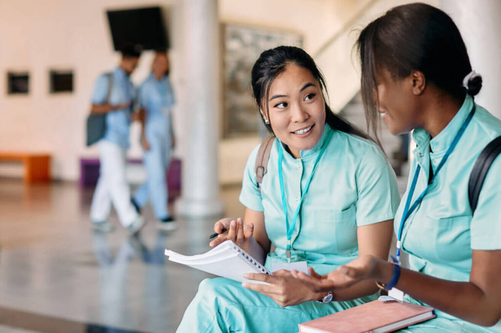 two female medical students sitting in a school building with notesbooks in their laps.