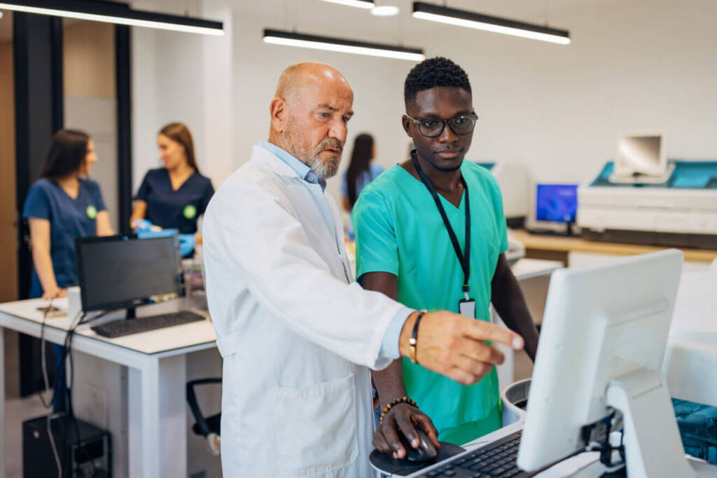 Two men in lab coats collaborating on computers in a laboratory setting.