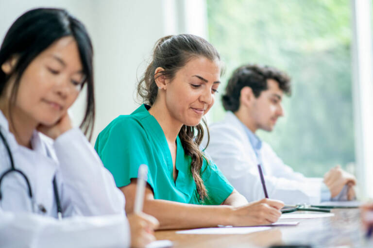 A group of doctors seated at a table, focused on writing notes and discussing medical topics.