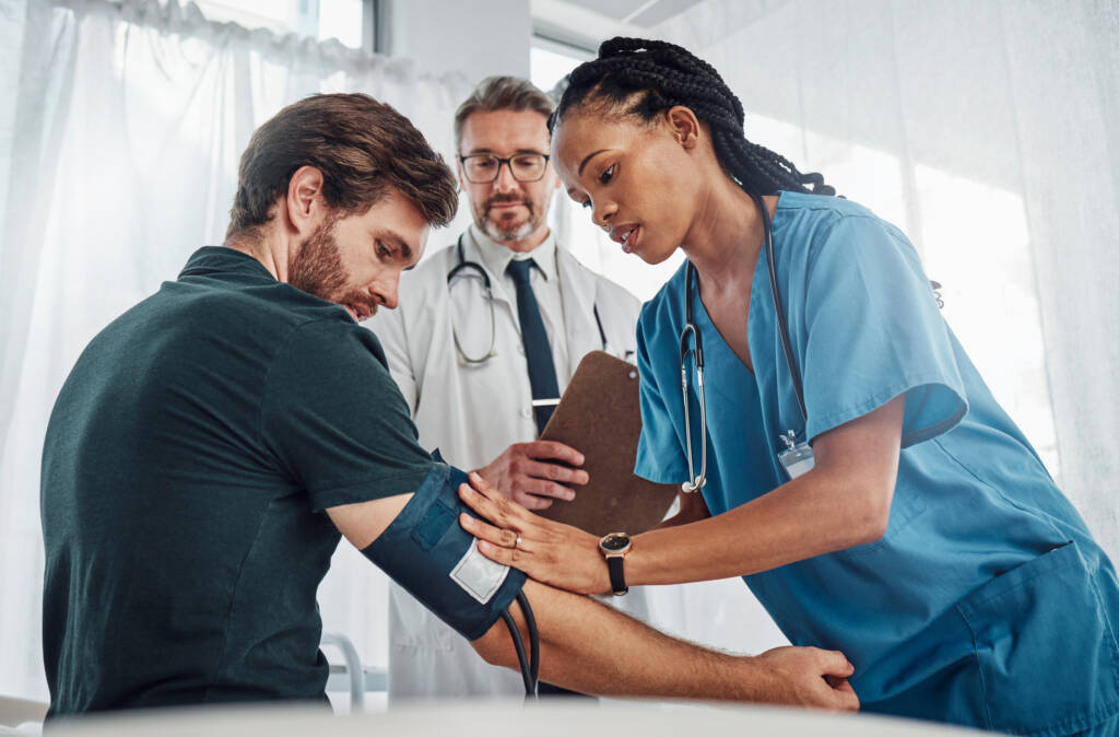A healthcare professional checks a patient's blood pressure with a cuff and monitor in a doctor's office.