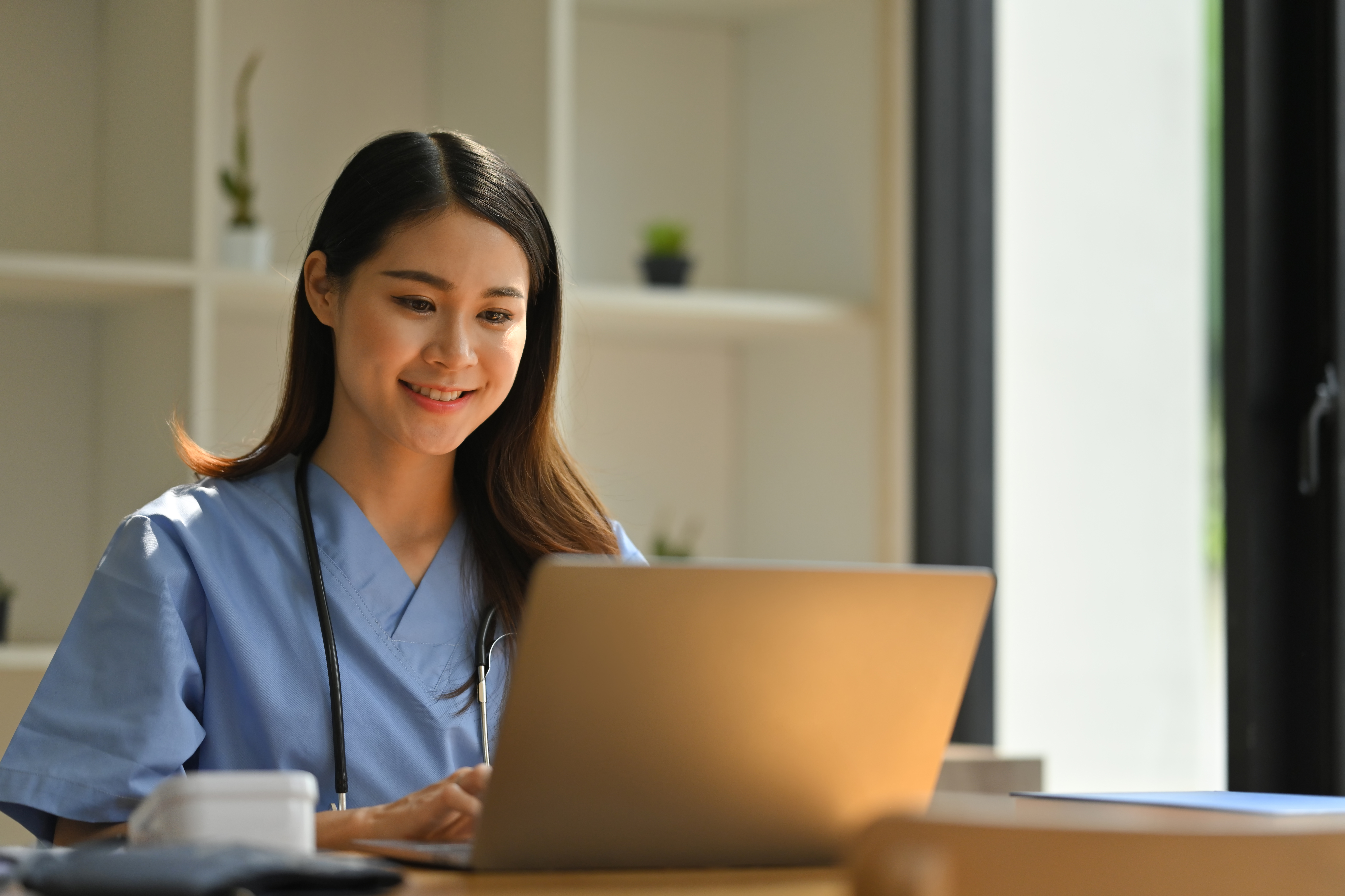 Smiling online medical assistant student completing course on laptop while sitting at modern workplace.
